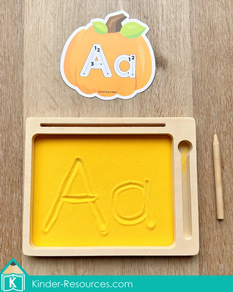 Pumpkin alphabet tracing card with uppercase and lowercase A beside a sand writing tray for preschool letter formation practice.