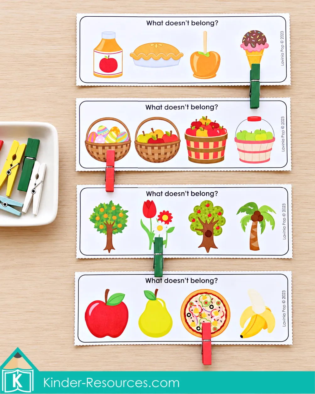 Apple centers for preschool with four What Doesn't Belong cards showing foods, baskets, trees, and fruit beside a dish of colored clothespins.