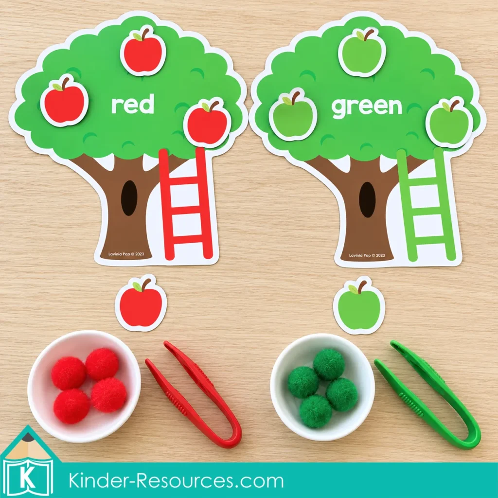 Apple centers for preschool with trees labeled red and green, matching apple cutouts, bowls of pom poms, and colored tweezers.