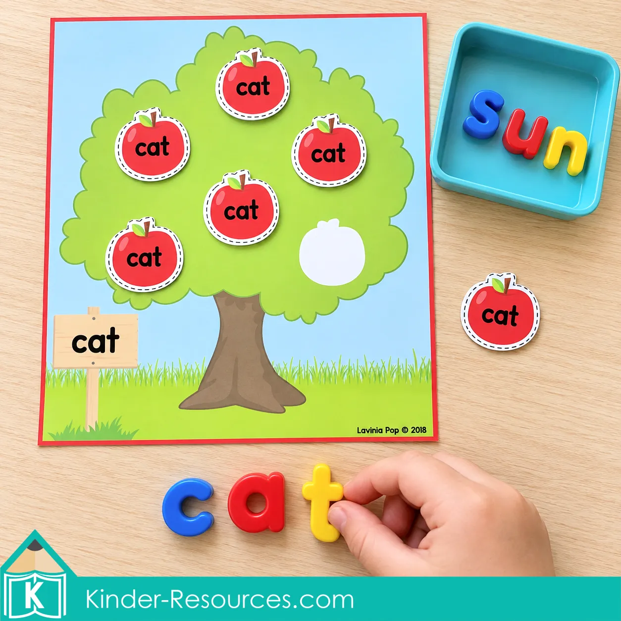 Child adding a magnetic letter t to spell “cat” beside an apple tree mat with matching “cat” word apples.
