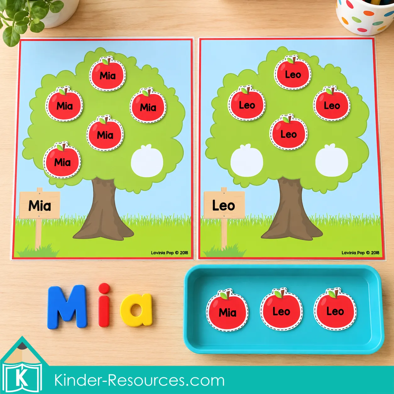 Apple tree mats labeled Mia and Leo with matching name apples, magnetic letters spelling Mia, and extra apples in a tray.