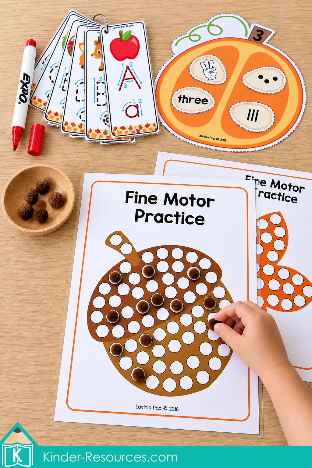 Child placing pom-poms on an acorn mat for fall preschool centers, with alphabet tracing cards and a pumpkin number match above.