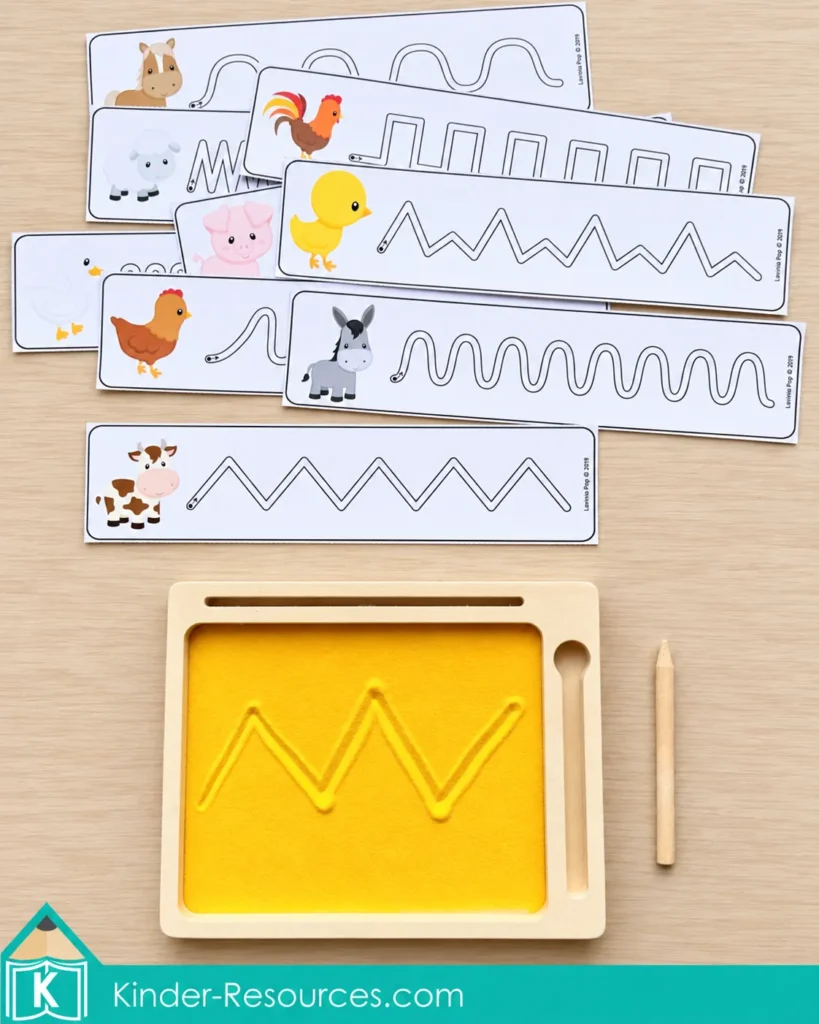 Farm animal tracing cards with curved and zigzag lines sit above a wooden sand tray containing a traced zigzag and a wooden stylus.